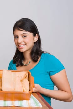 Portrait of a young woman smiling with a tray of breads in the kitchen