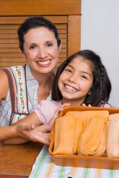 Portrait of a girl and her mother smiling with a tray of breads in the kitchen