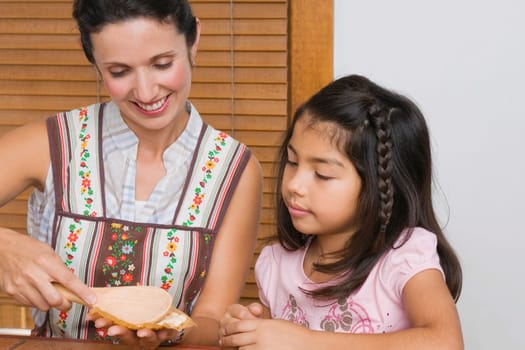 Mid adult woman preparing bread with her daughter in the kitchen