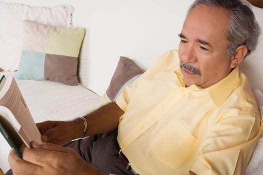 High angle view of a senior man sitting on a couch and holding a book