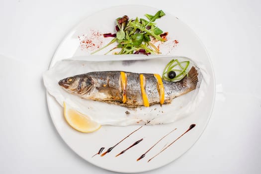 Fried fish with lemon on a white plate. Dandelion salad.
