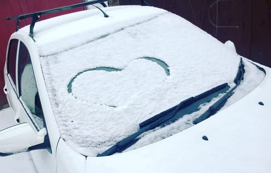 Painted heart in the snow by car in winter.
