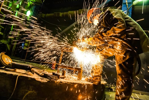 The welder cooks a steel structure. Sparks are flying. The work of a welder.