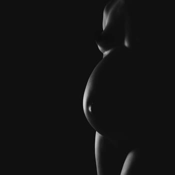 Nude pregnant woman in shadow and side lighting.