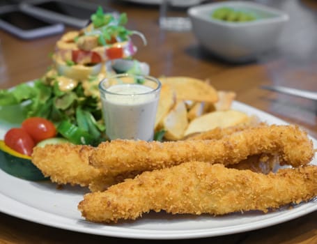 Fish and chips on white plate. Deep fried fish filets and French fries served with tarter sauce and green salad