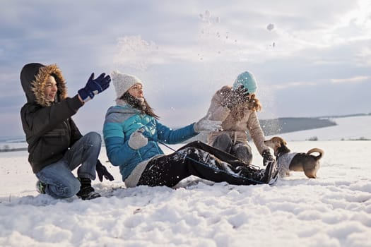 family walks the small dog in woolen clothes in the snow during winter time