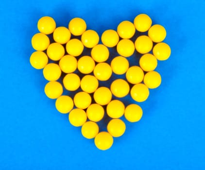Small medical pharmaceptic round yellow pills, vitamins, drugs, antibiotics in the form of a heart on a blue background, texture. Concept: medicine, health care, heart disease.