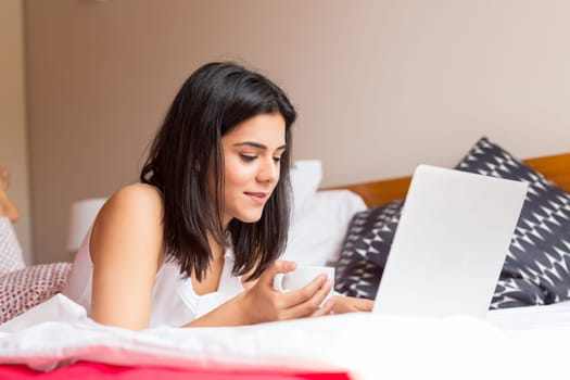 Young woman relaxing with her computer in bed