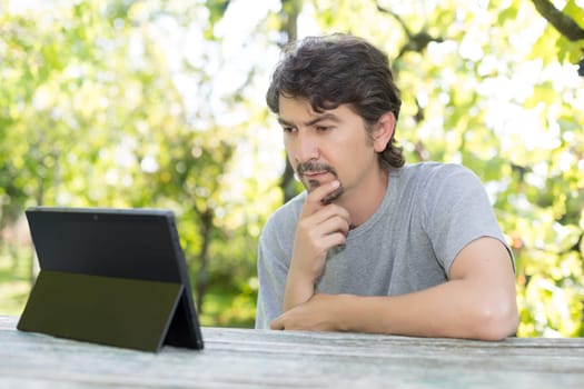 Young man relaxing with a touchscreen computer at a garden