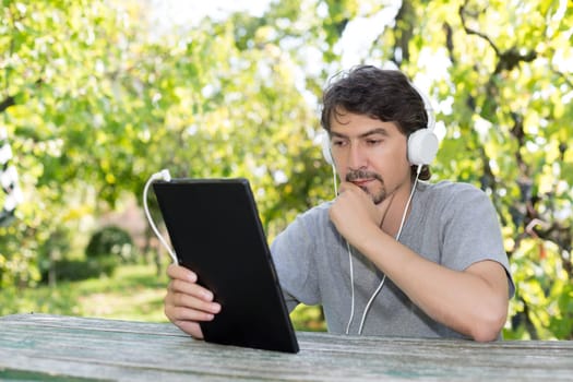 Young man relaxing with a touchscreen computer at a garden