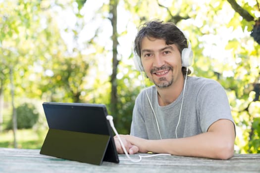 Young man relaxing with a touchscreen computer at a garden