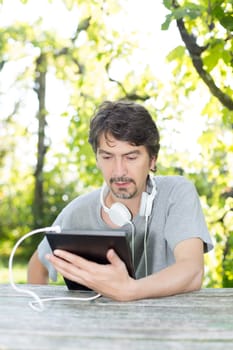 Young man relaxing with a touchscreen computer at a garden