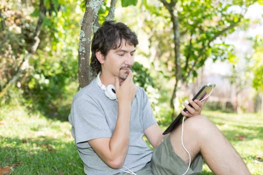 Young man relaxing with a touchscreen computer at a garden