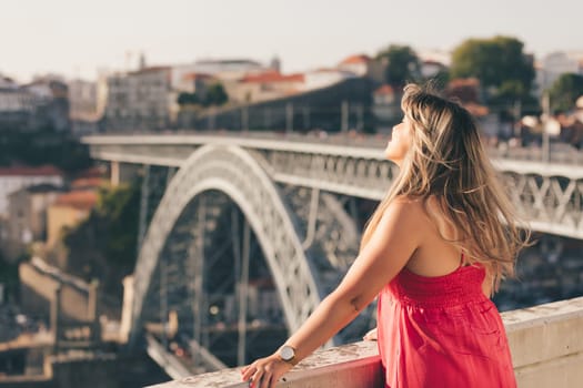 Young woman tourist enjoying beautiful landscape view on the old town with river and famous iron bridge during the sunset in Porto city, Portugal