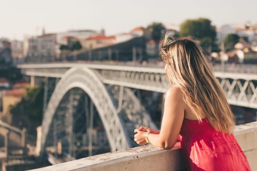 Young woman tourist enjoying beautiful landscape view on the old town with river and famous iron bridge during the sunset in Porto city, Portugal