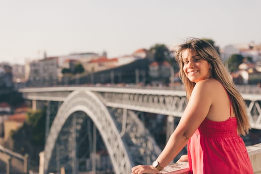 Young woman tourist enjoying beautiful landscape view on the old town with river and famous iron bridge during the sunset in Porto city, Portugal