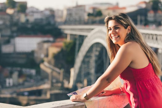 Young woman tourist enjoying beautiful landscape view on the old town with river and famous iron bridge during the sunset in Porto city, Portugal