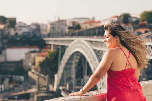 Young woman tourist enjoying beautiful landscape view on the old town with river and famous iron bridge during the sunset in Porto city, Portugal