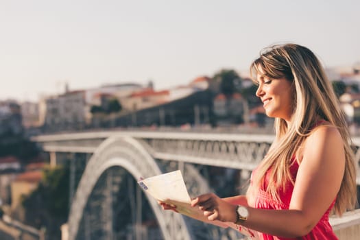 Young woman tourist enjoying beautiful landscape view on the old town with river and famous iron bridge during the sunset in Porto city, Portugal