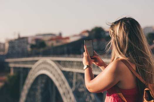 Young woman tourist enjoying beautiful landscape view on the old town with river and famous iron bridge during the sunset in Porto city, Portugal
