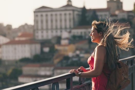 Young woman tourist enjoying beautiful landscape view on the old town with river and famous iron bridge during the sunset in Porto city, Portugal