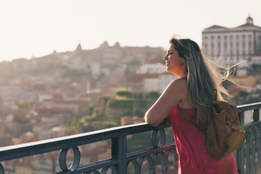 Young woman tourist enjoying beautiful landscape view on the old town with river and famous iron bridge during the sunset in Porto city, Portugal