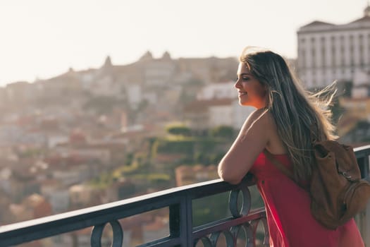 Young woman tourist enjoying beautiful landscape view on the old town with river and famous iron bridge during the sunset in Porto city, Portugal