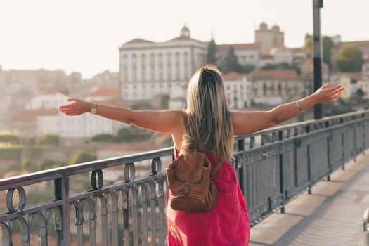 Young woman tourist enjoying beautiful landscape view on the old town with river and famous iron bridge during the sunset in Porto city, Portugal