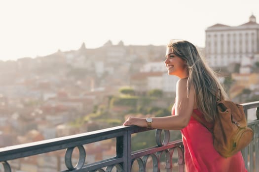 Young woman tourist enjoying beautiful landscape view on the old town with river and famous iron bridge during the sunset in Porto city, Portugal