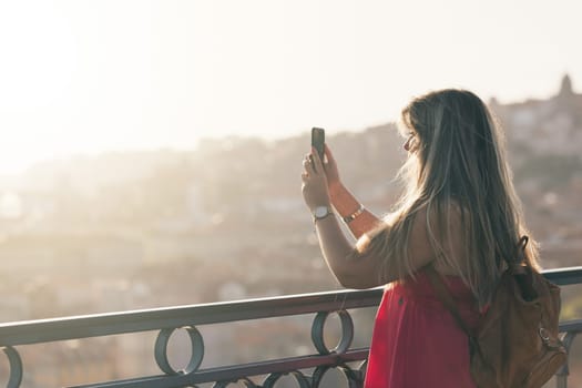 Young woman tourist enjoying beautiful landscape view on the old town with river and famous iron bridge during the sunset in Porto city, Portugal