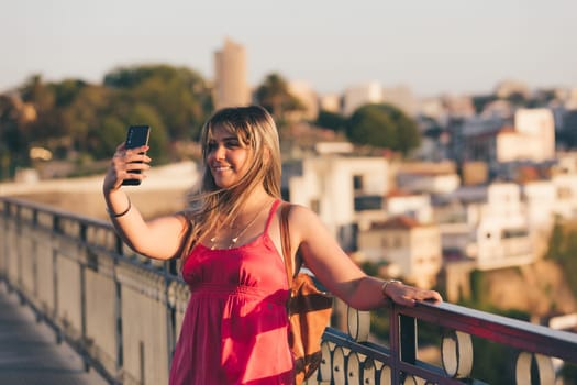 Young woman tourist enjoying beautiful landscape view on the old town with river and famous iron bridge during the sunset in Porto city, Portugal