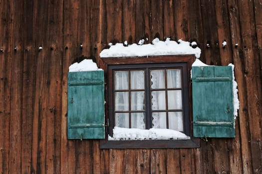 A window with green shutters on an old farmhouse in winter with snow