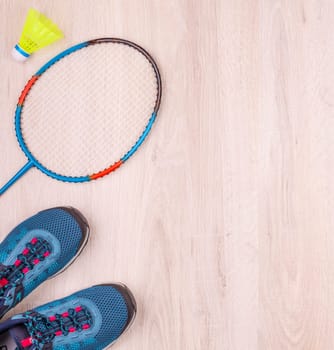 Pair of blue women's sneakers, badminton racket and shuttlecock on white wooden surface