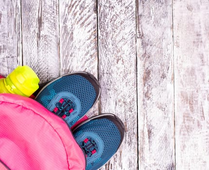 Pair of blue women's sneakers in pink backpack and sports bottle for a water on white wooden surface