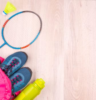 Pair of blue women's sneakers and bottle in pink backpack, badminton racket and shuttlecock on white wooden surface