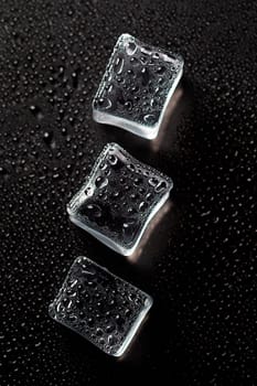 Three Ice cubes on black color texture. Concept art. Minimal surrealism. Flat lay with copy space. Soft focus. Vertical orientation.