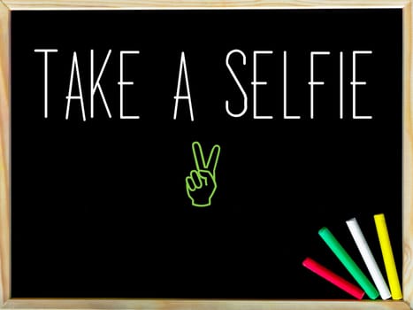 Take a Selfie message and Peace sign.Handwriting with chalk on wooden frame blackboard, colored chalk in the corner, Fun concept image