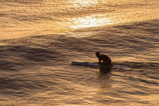 Lifeguard  athlete trains dawn sunrise on rescue craft paddling out through ocean wave swells.