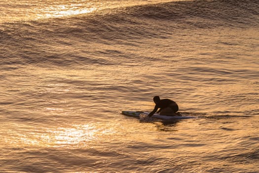 Lifeguard  athlete trains dawn sunrise on rescue craft paddling out through ocean wave swells.