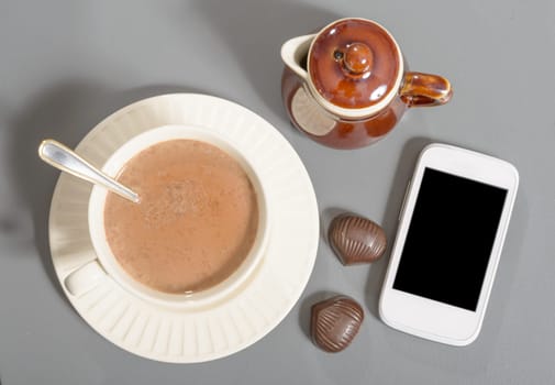 cup of hot chocolate with a phone on a grey table