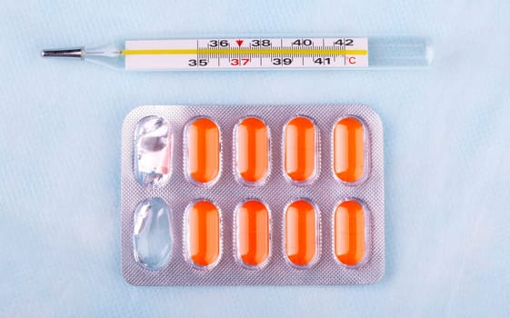 The pills in red packaging and thermometer on blur medical background