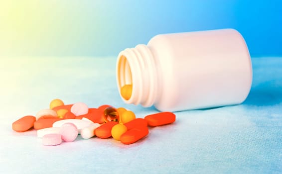 colorful pills of medicine from a plastic drug bottle on blue background