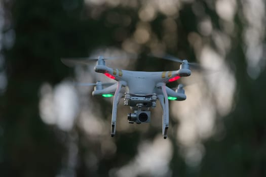 1 - Drone quadcopter hovering in front of trees, blurred background of defocused trees at sunset
