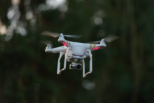 6 - Common white camera drone used for surveillance, plain background. Logos all removed, propellers blurred from moving at high speed