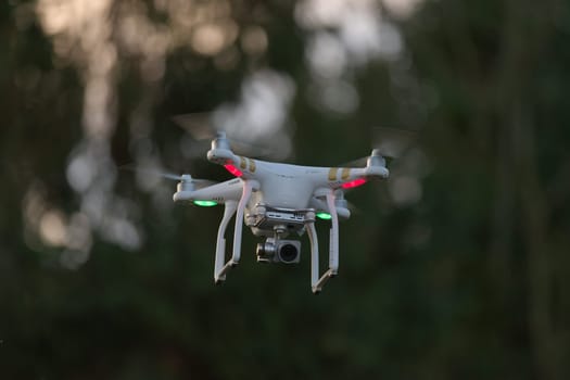 Flying quad copter UAV drone hovering with defocused tree background. Taken during golden hour in the evening at sunset.