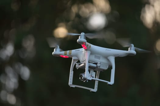 16 - Professional camera on a silver gimbal carried by a white drone. Taken at evening time in a rural location, with a defocused background of trees