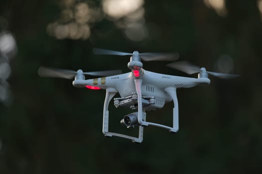 17 - White quad copter drone with red lights on a dark background. Unmanned ariel vehicle with camera gimbal payload used for filming video or photos