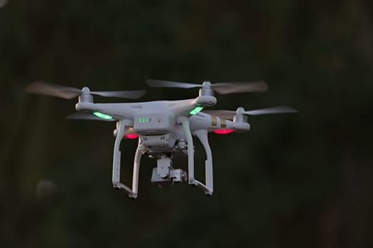 25 - Rear view of professional quadcopter camera drone hovering. Looking from behind shows the battery status indicator lights and green orientation.