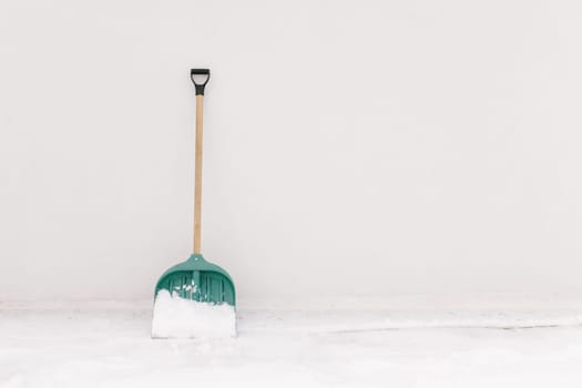 Snow shovel propped against the white wall of the house. High quality photo