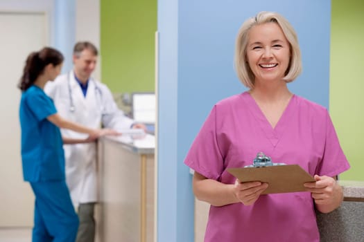Female nurse holding a clipboard with a doctor and a nurse in the background